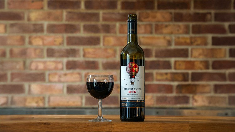 An image of a Shiraz wine bottle made in Barossa Valley, sitting adjacent to a glass of wine